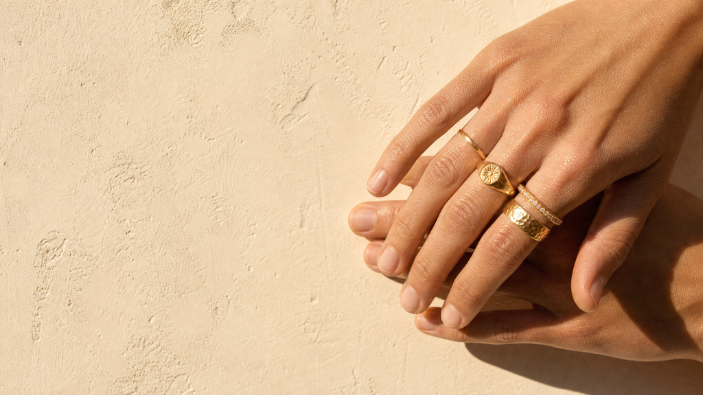 Stacked 18k gold rings worn on a hand against a warm plaster wall
