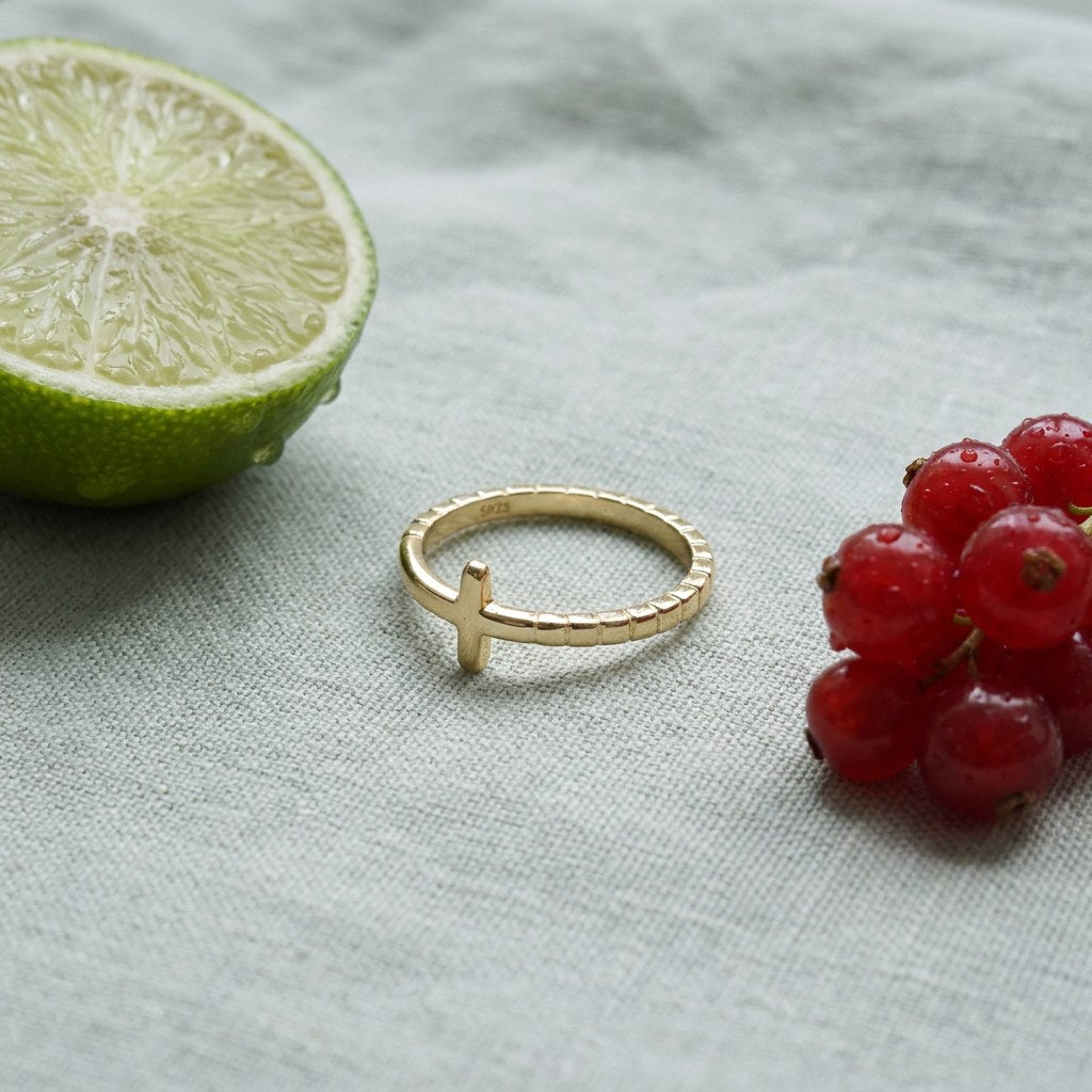 Gold Plated Cross Ring in Stainless Steel on pale grey-green linen beside a halved lime and red currants
