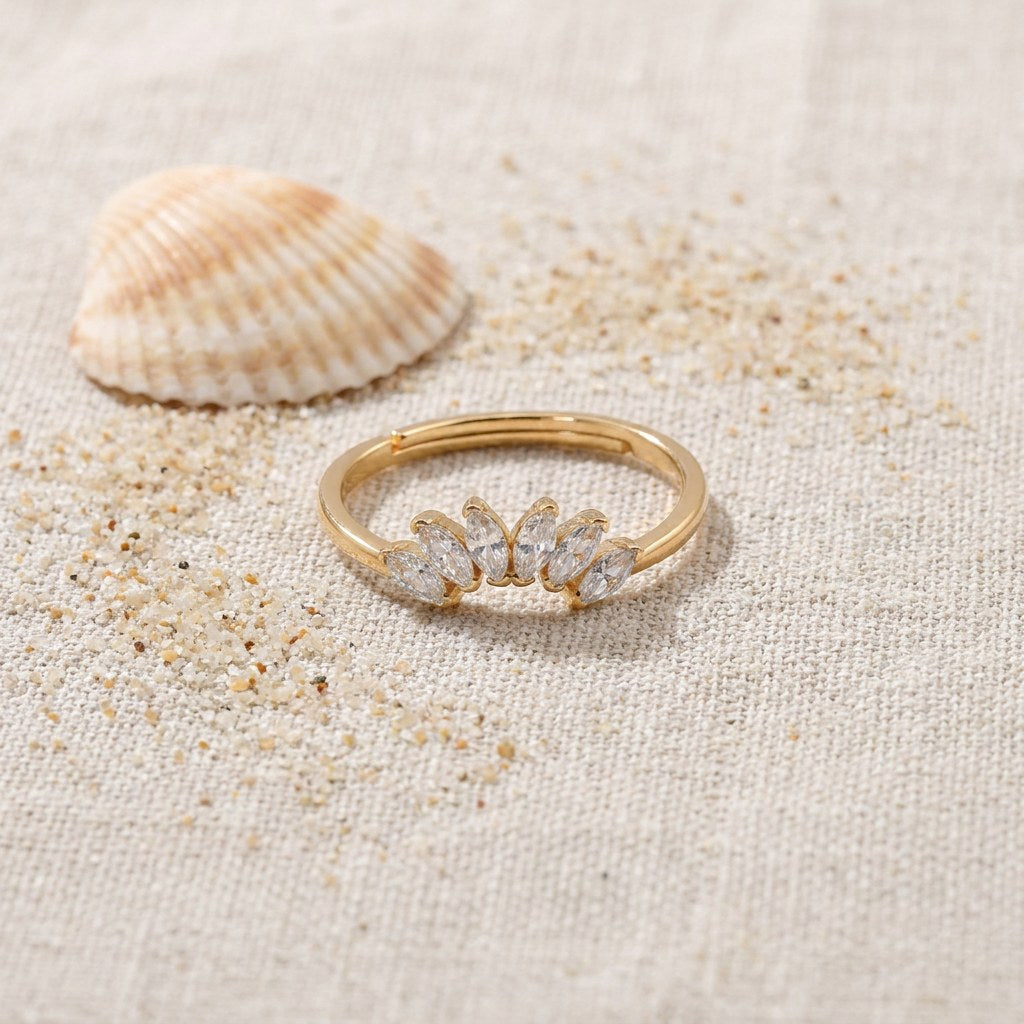 Contour Gemstone Band Ring on raw linen beside a scallop shell and a scatter of fine sand