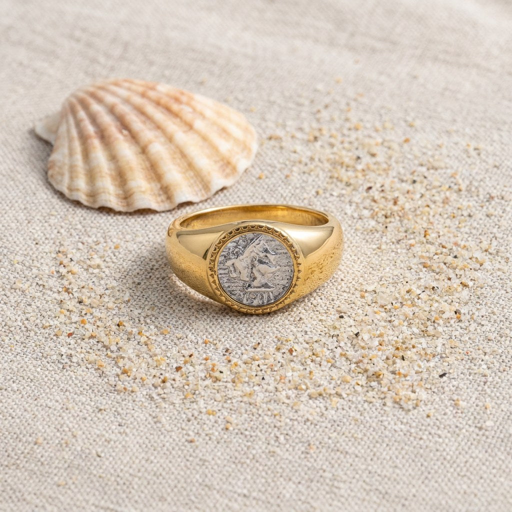 Athena Coin Signet Ring on raw linen beside a scallop shell and a scatter of fine sand