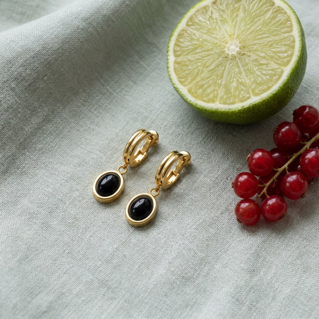 Black Onyx Drop Hoop Earrings on pale grey-green linen beside a halved lime and red currants