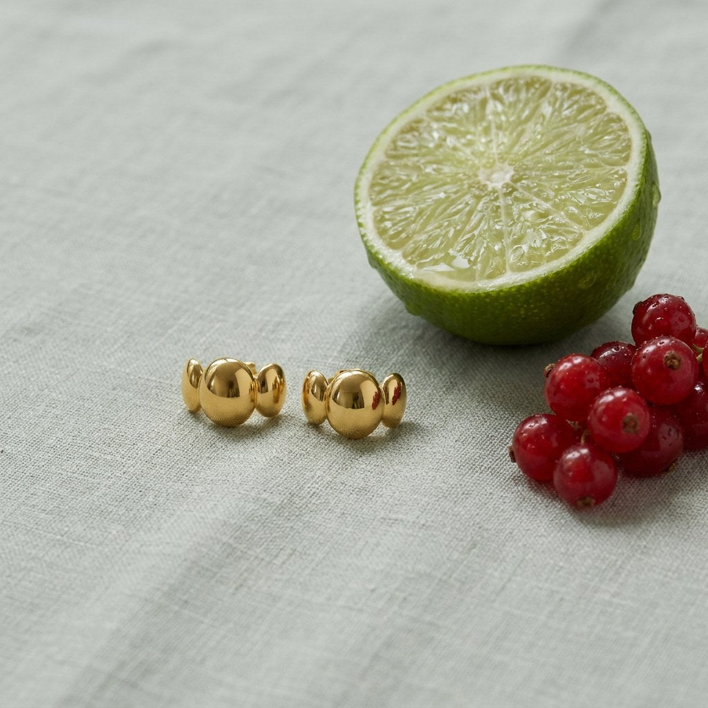 Bubble Stud Earrings on pale grey-green linen beside a halved lime and red currants