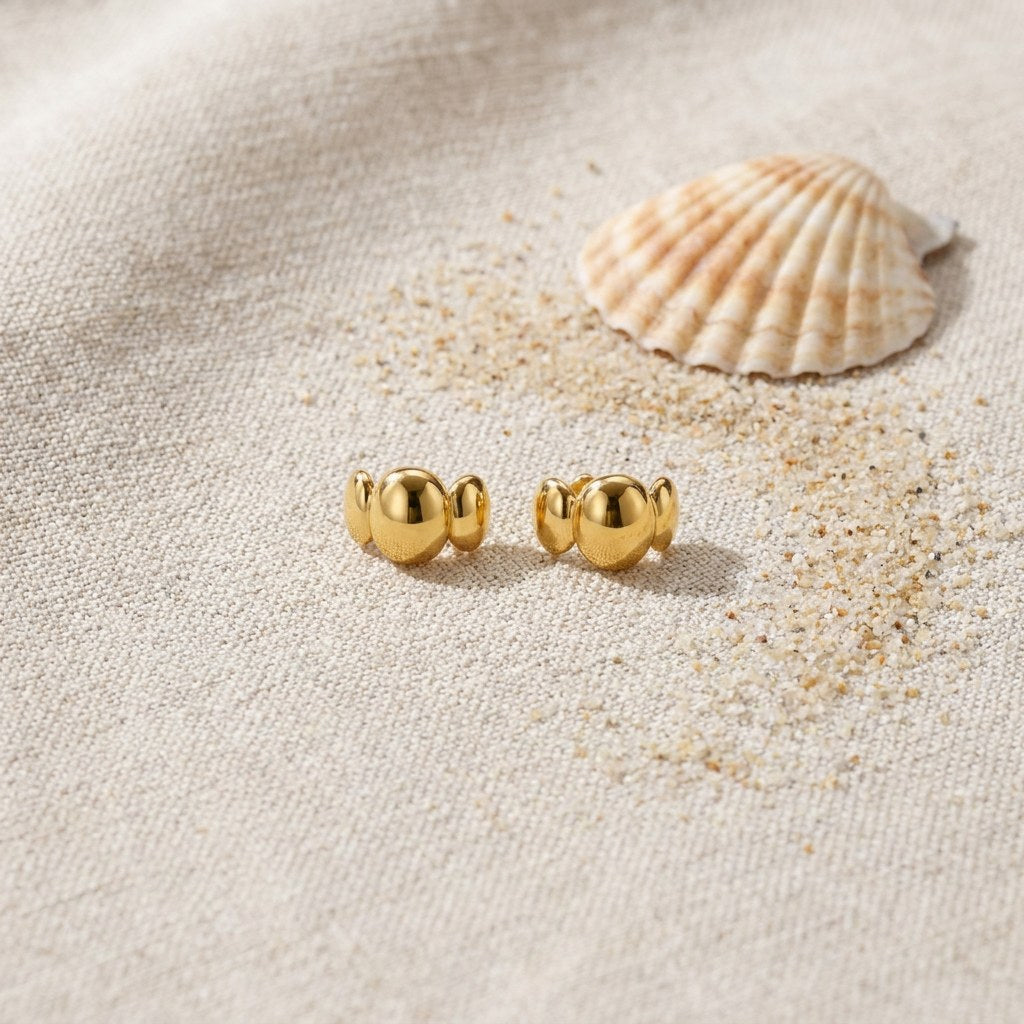 Bubble Stud Earrings on raw linen beside a scallop shell and a scatter of fine sand