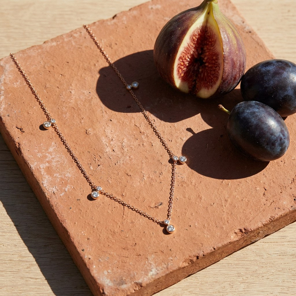 Crystal Bezel Station Necklace on a weathered terracotta tile with a cut fig and dark plums