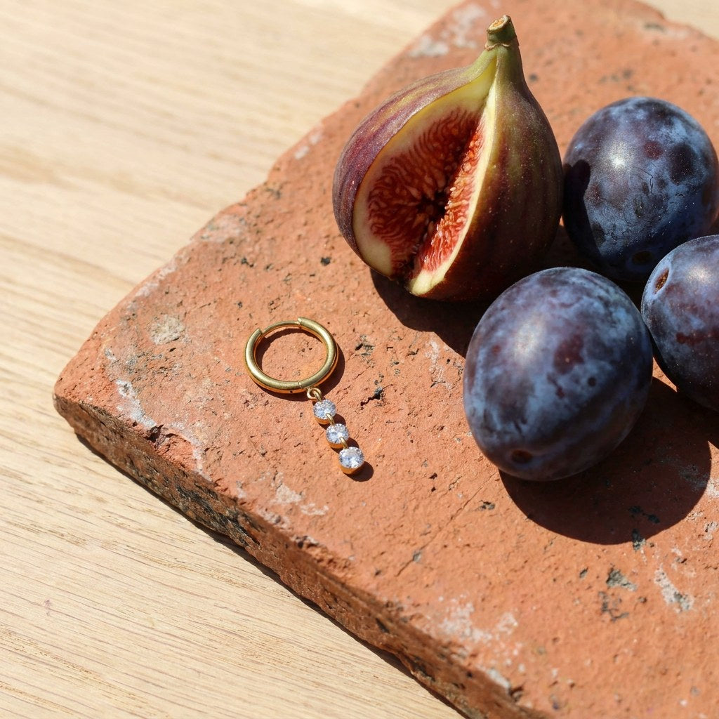 Crystal Drop Hoop Earrings on a weathered terracotta tile with a cut fig and dark plums