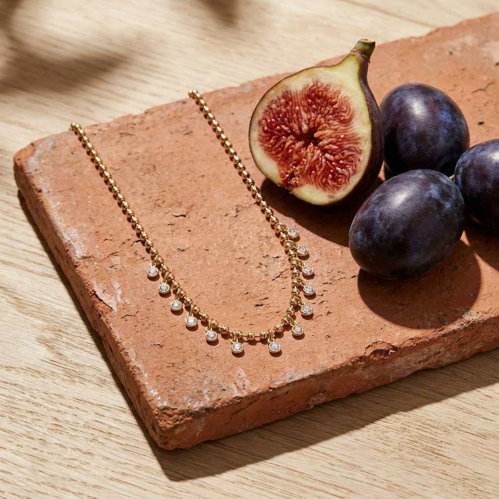 Crystal Fringe Necklace on a weathered terracotta tile with a cut fig and dark plums