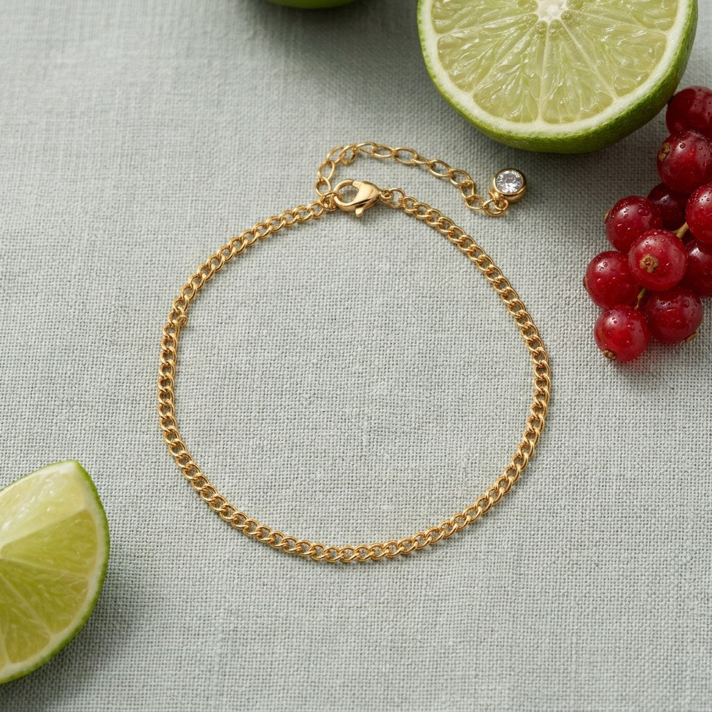 Curb Chain Anklet on pale grey-green linen beside a halved lime and red currants