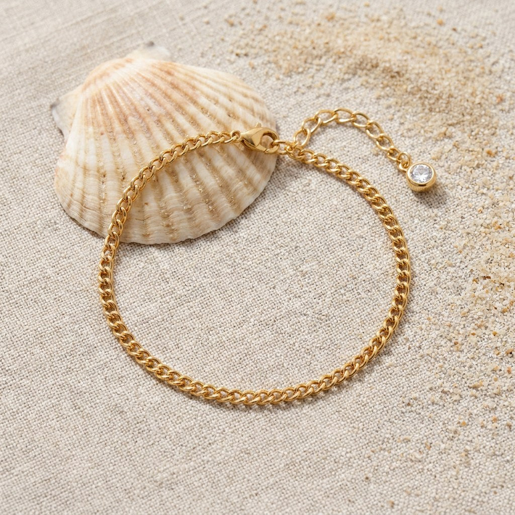 Curb Chain Anklet on raw linen beside a scallop shell and a scatter of fine sand