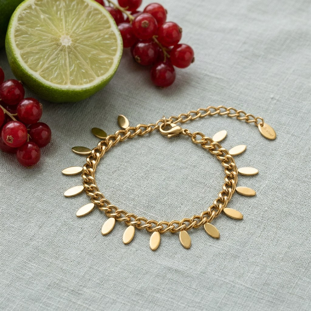 Dainty Gold Tassel Chain Bracelet on pale grey-green linen beside a halved lime and red currants