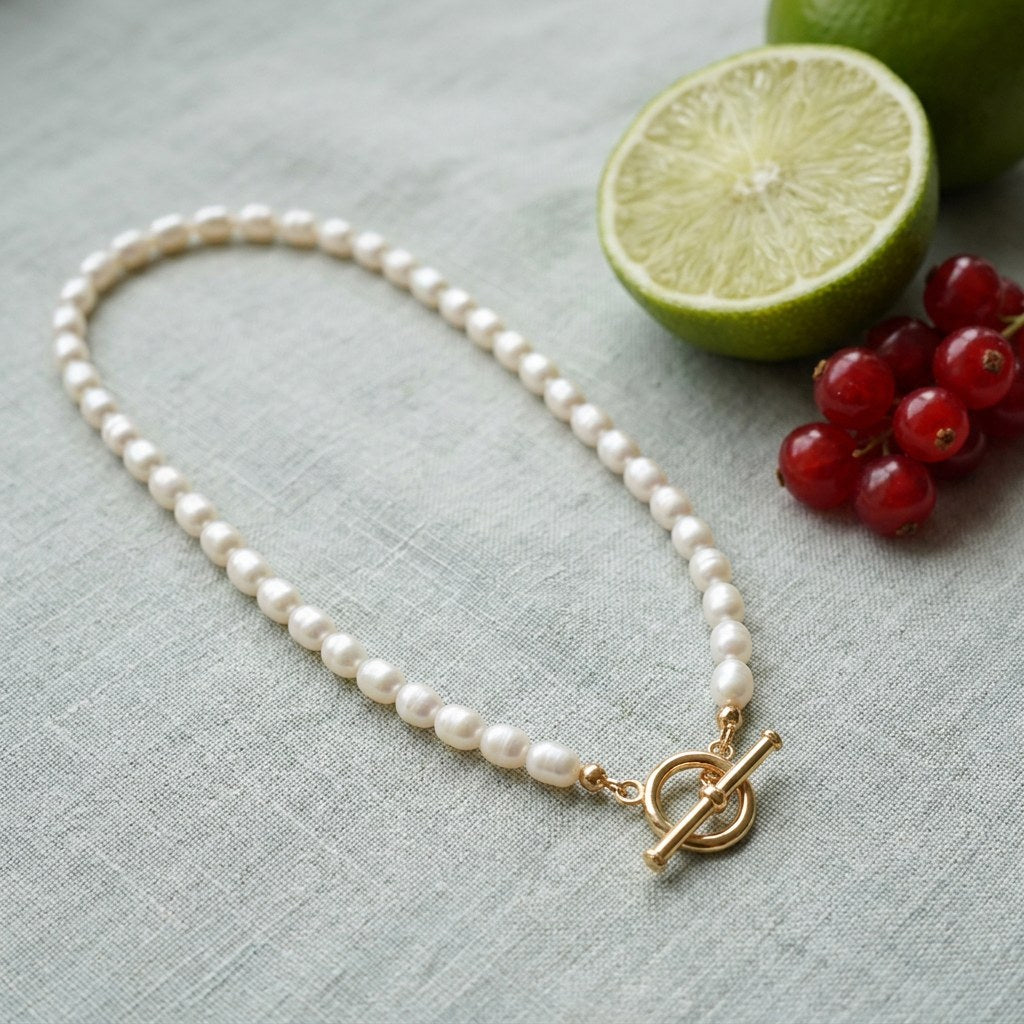 Dainty Pearl Toggle Necklace on pale grey-green linen beside a halved lime and red currants