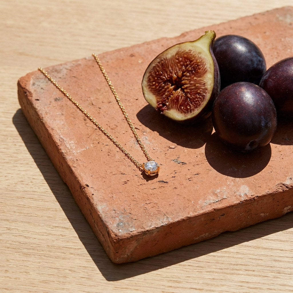 Dainty Solitaire Necklace on a weathered terracotta tile with a cut fig and dark plums