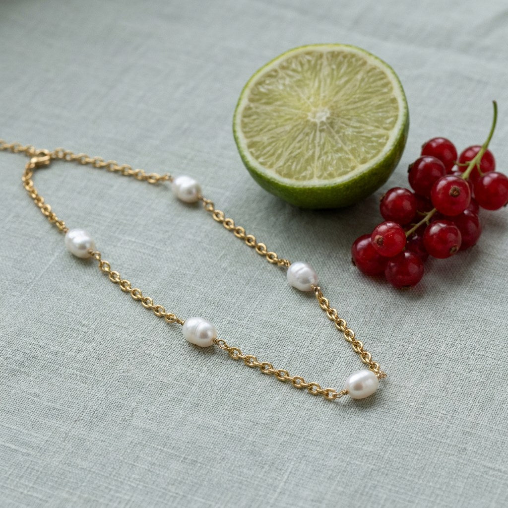 Freshwater Pearl Station Necklace on pale grey-green linen beside a halved lime and red currants