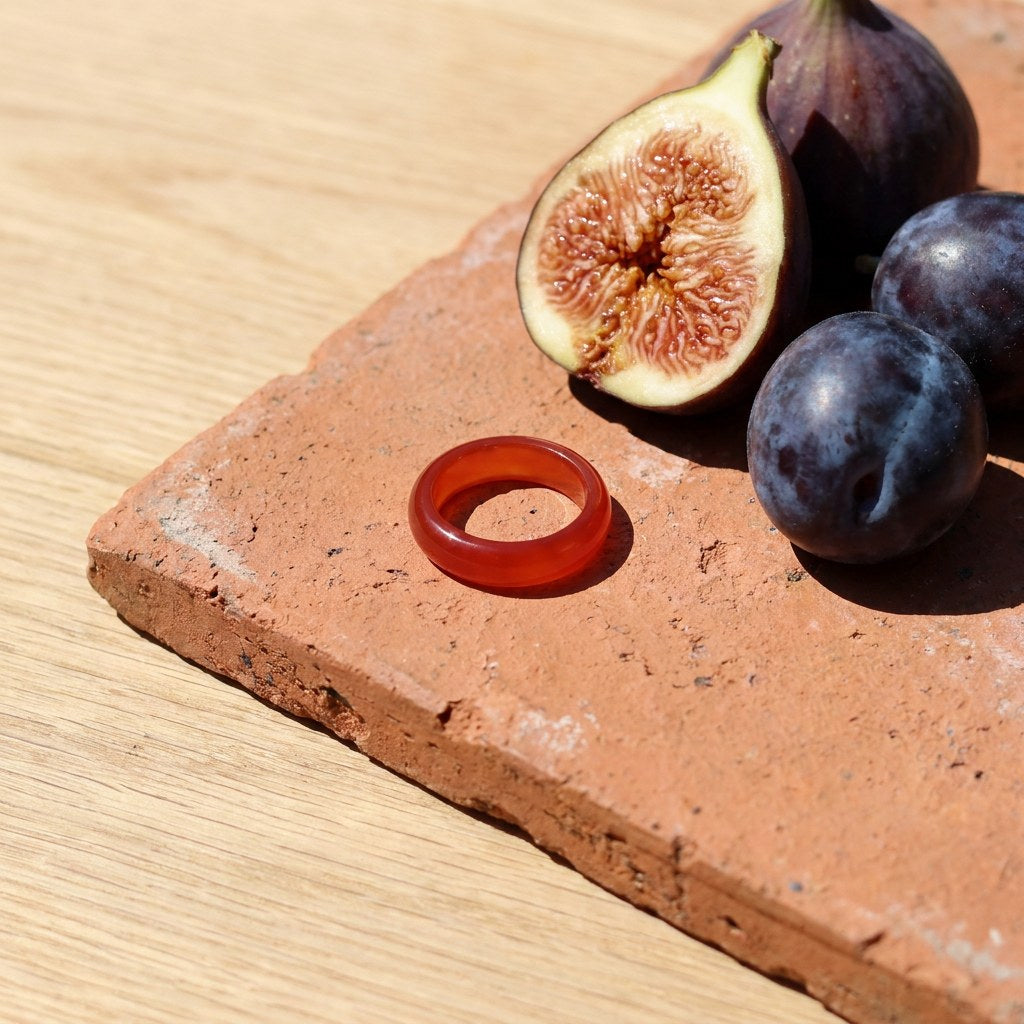 Genuine Red Jade Band Ring on a weathered terracotta tile with a cut fig and dark plums
