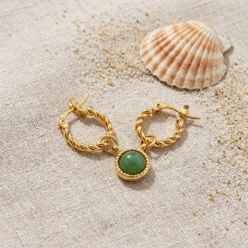 Green Jade Hoop Earrings on raw linen beside a scallop shell and a scatter of fine sand