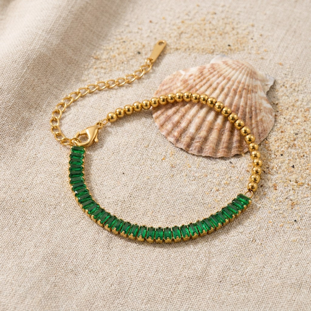 Half Emerald Half Beaded Bracelet on raw linen beside a scallop shell and a scatter of fine sand