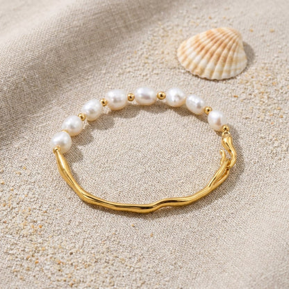 Half Pearl Gold Bracelet on raw linen beside a scallop shell and a scatter of fine sand