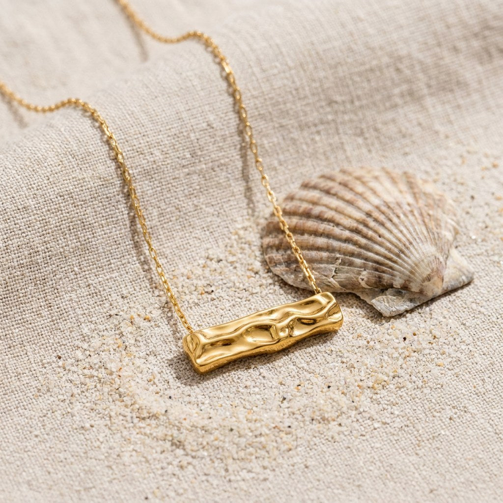 Hammered Rectangle Necklace on raw linen beside a scallop shell and a scatter of fine sand