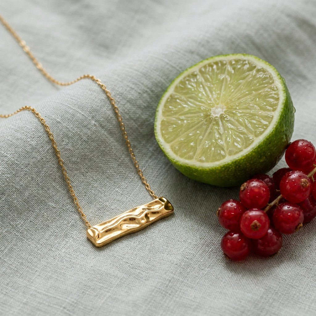 Hammered Rectangle Necklace on pale grey-green linen beside a halved lime and red currants