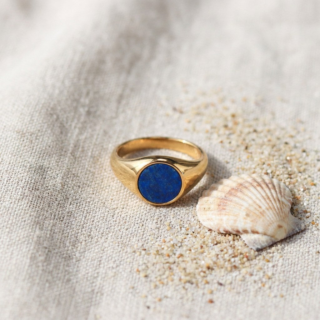 Lapis Lazuli Signet Ring on raw linen beside a scallop shell and a scatter of fine sand