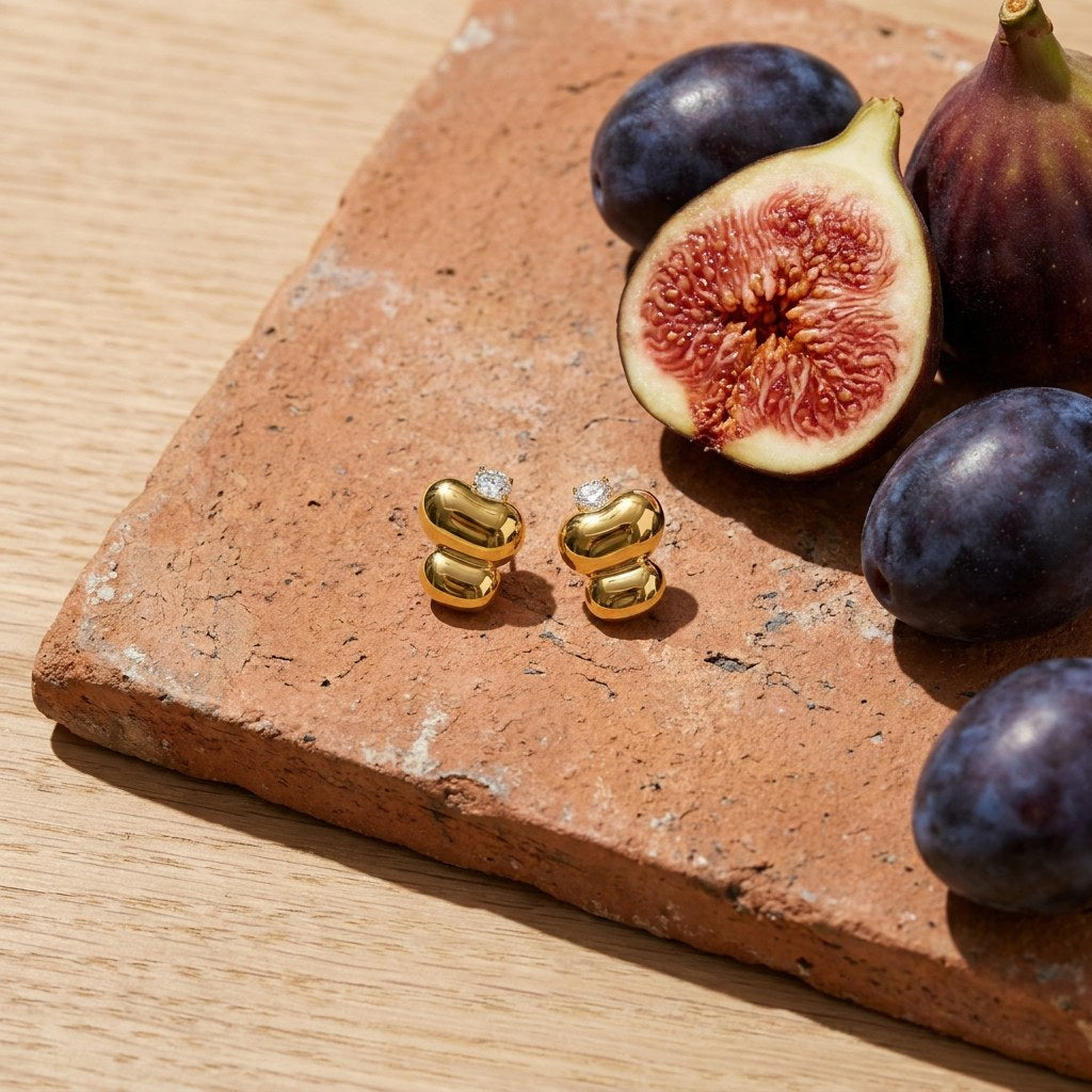 Molten Stud Earrings on a weathered terracotta tile with a cut fig and dark plums