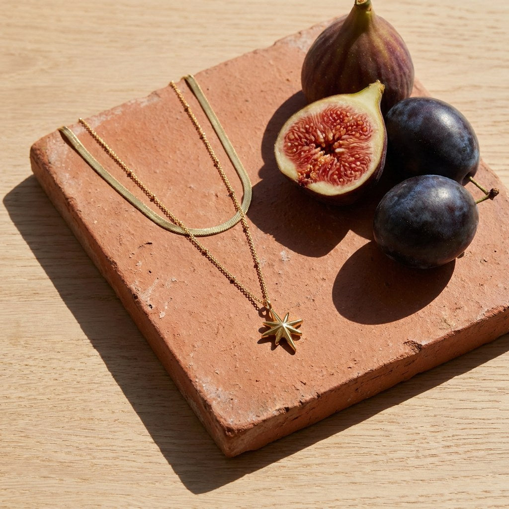 North Star Layered Necklace on a weathered terracotta tile with a cut fig and dark plums