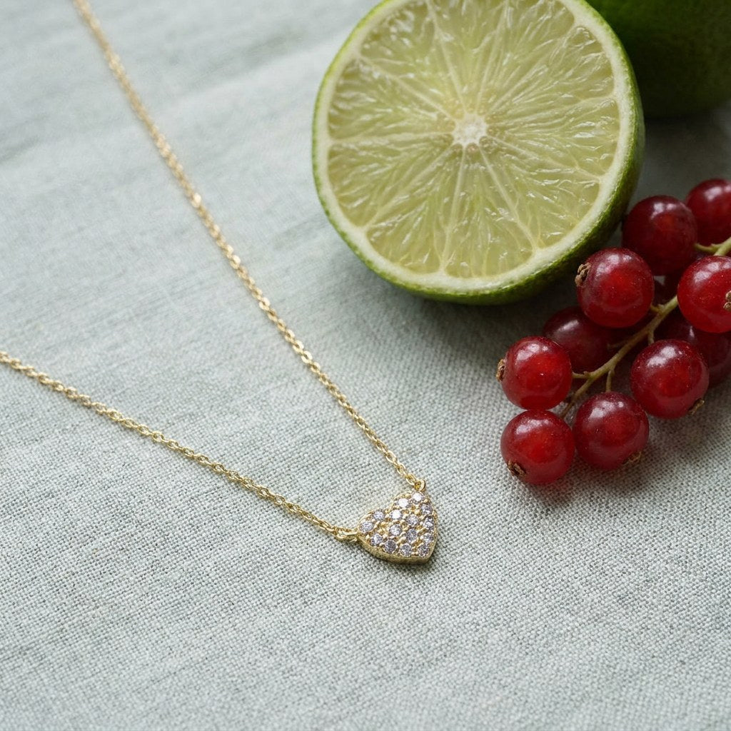 Pave Little Heart Necklace on pale grey-green linen beside a halved lime and red currants