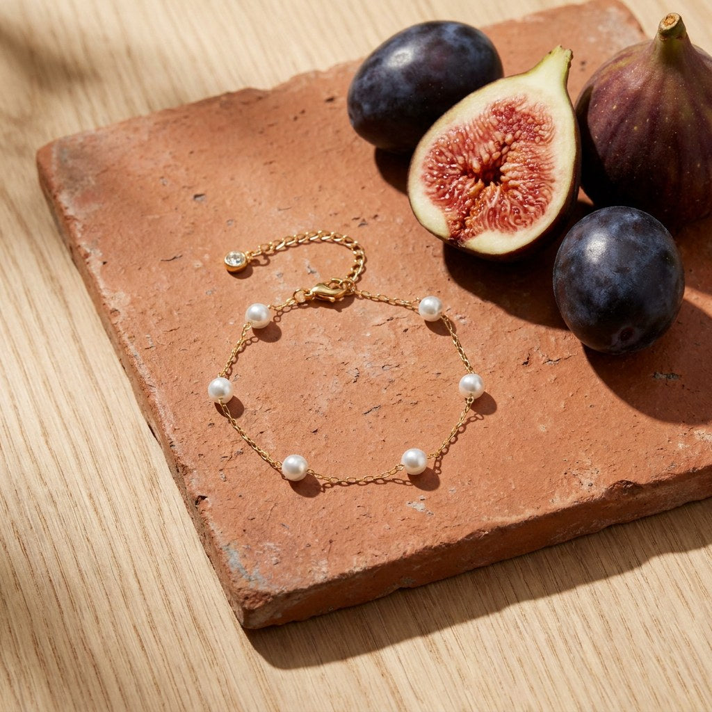 Pearl Station Anklet on a weathered terracotta tile with a cut fig and dark plums