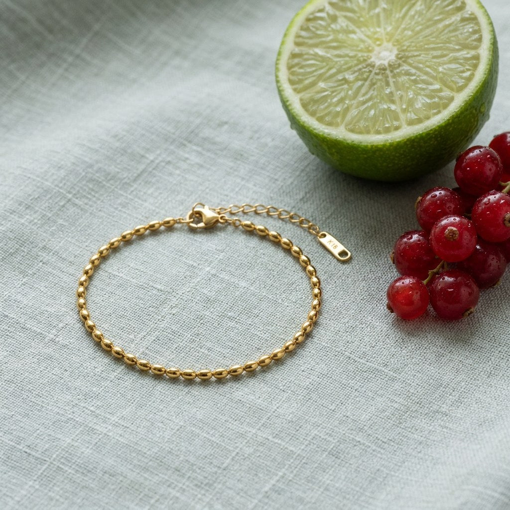 Rice Bead Anklet on pale grey-green linen beside a halved lime and red currants