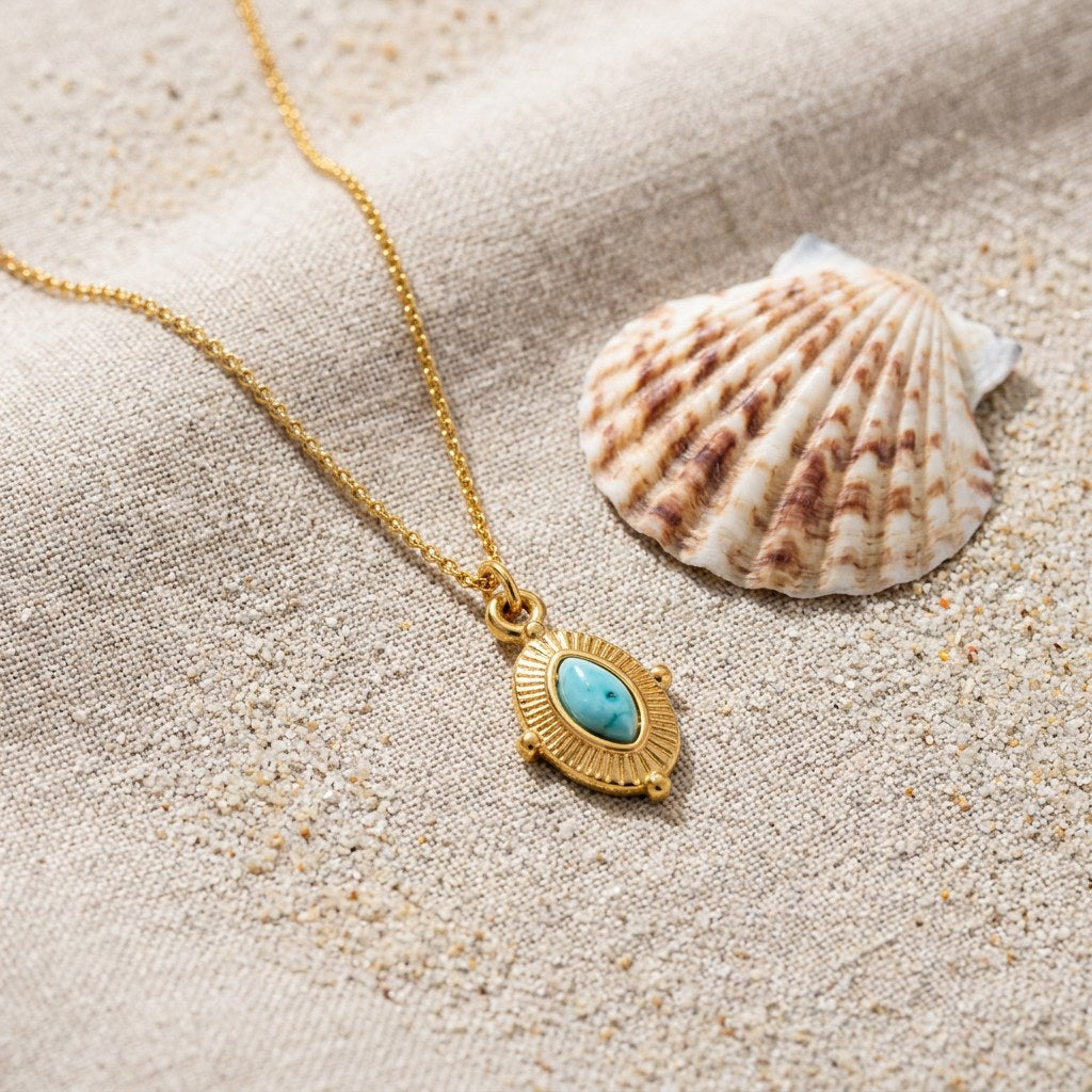 Royal Marquise Turquoise Necklace on raw linen beside a scallop shell and a scatter of fine sand