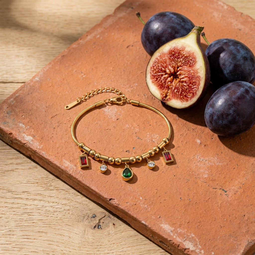 Ruby and Emerald Charm Bracelet on a weathered terracotta tile with a cut fig and dark plums