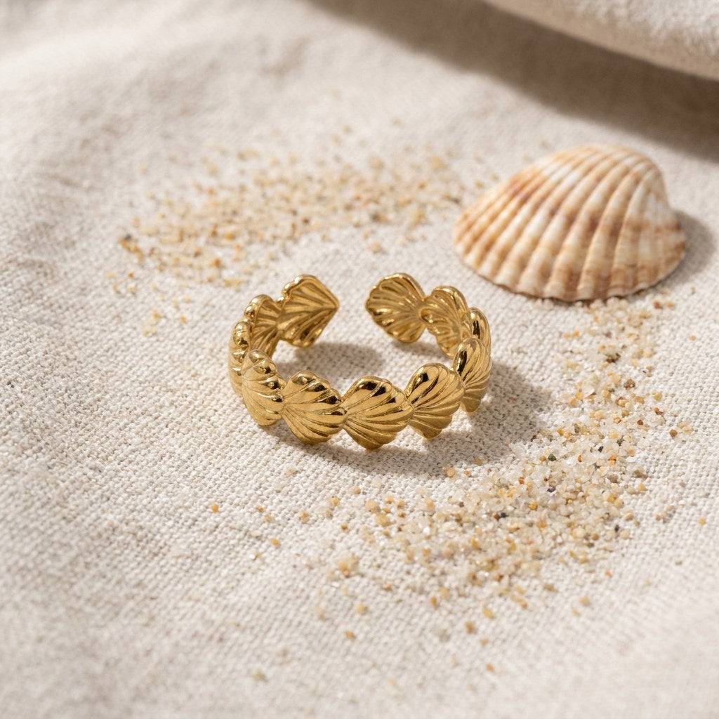 Scallop Shell Band Ring on raw linen beside a scallop shell and a scatter of fine sand