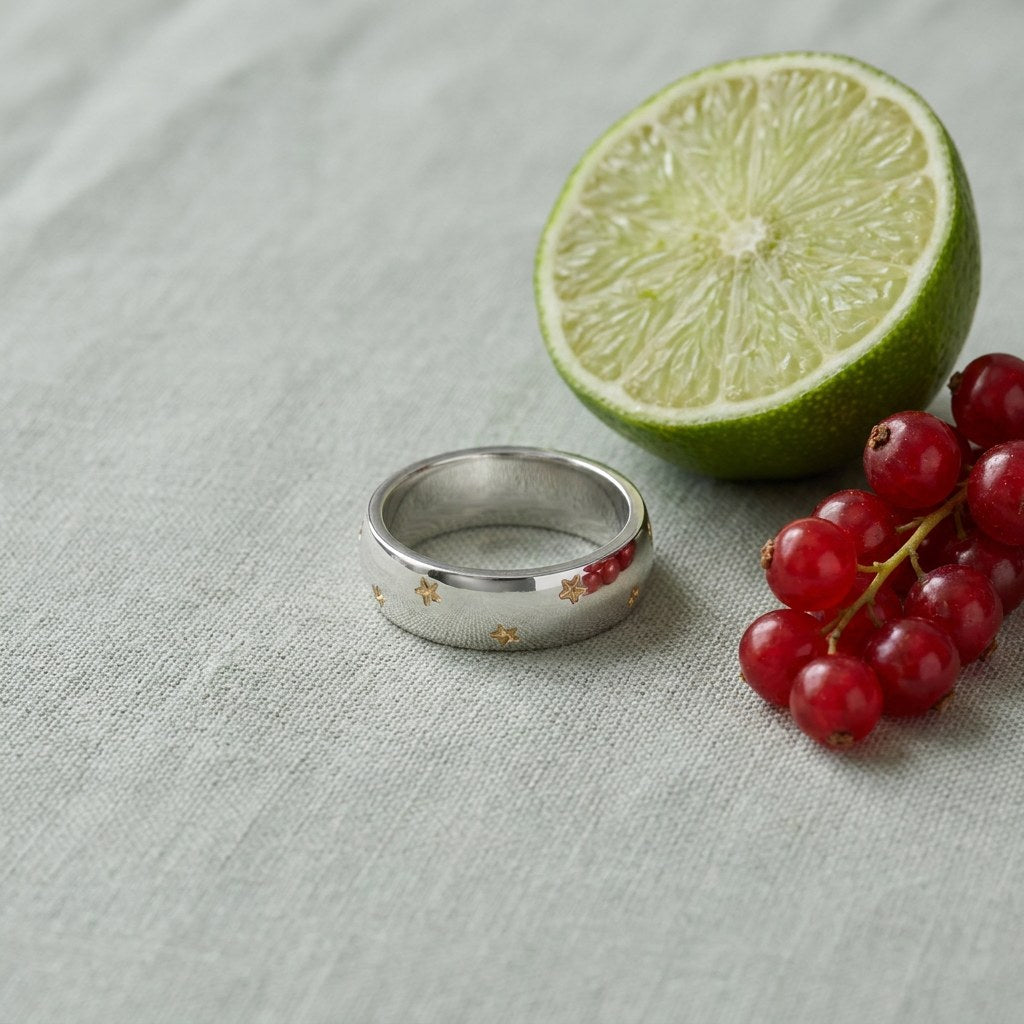 Silver Starburst Band Ring on pale grey-green linen beside a halved lime and red currants