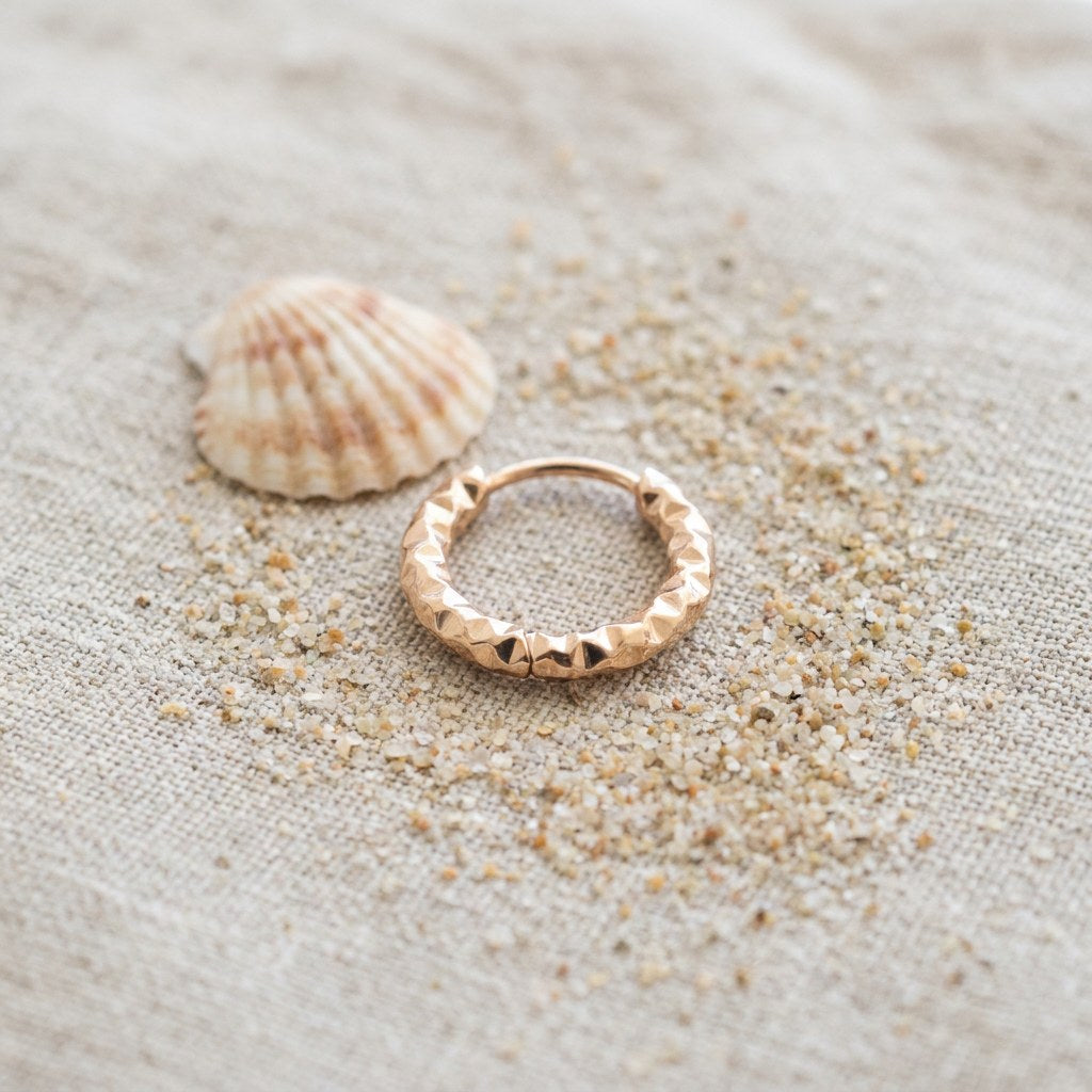 Small Hammered Hoop Earrings in Gold Stainless Steel on raw linen beside a scallop shell and a scatter of fine sand