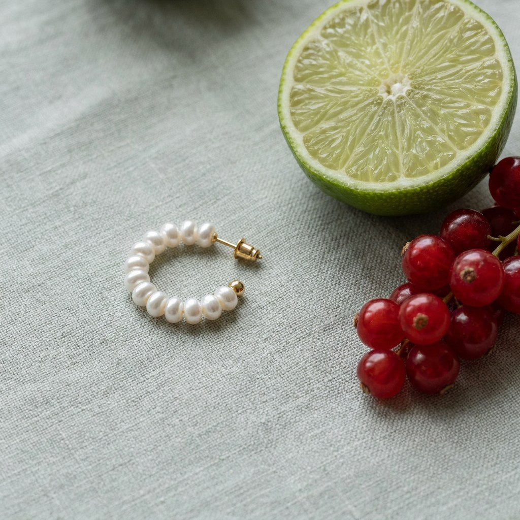 Small Pearl Hoop Earrings on pale grey-green linen beside a halved lime and red currants