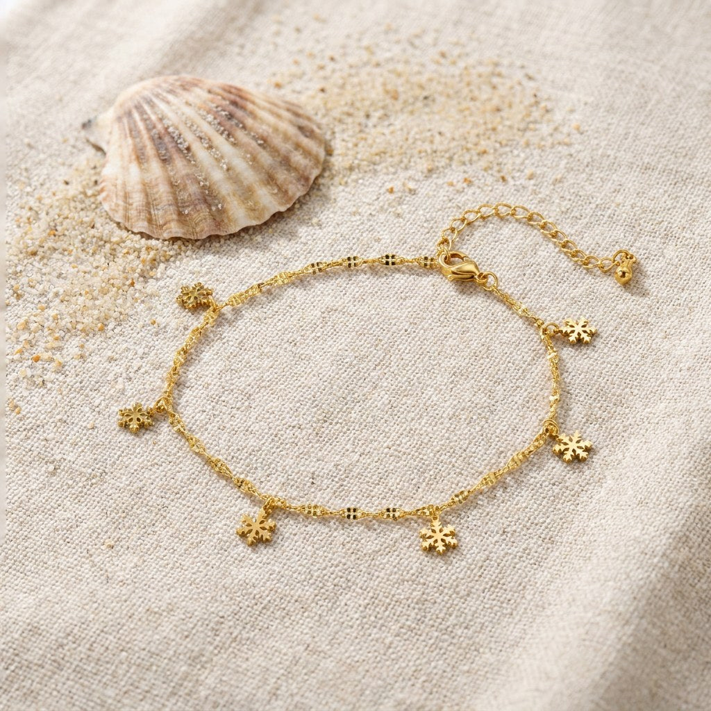 Snowflake Anklet on raw linen beside a scallop shell and a scatter of fine sand