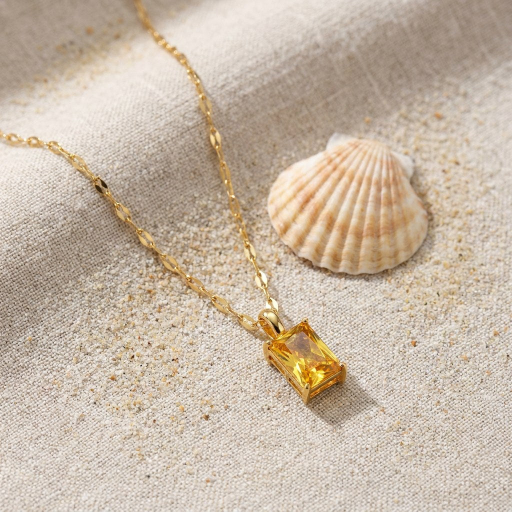 Solar Pendant Necklace on raw linen beside a scallop shell and a scatter of fine sand