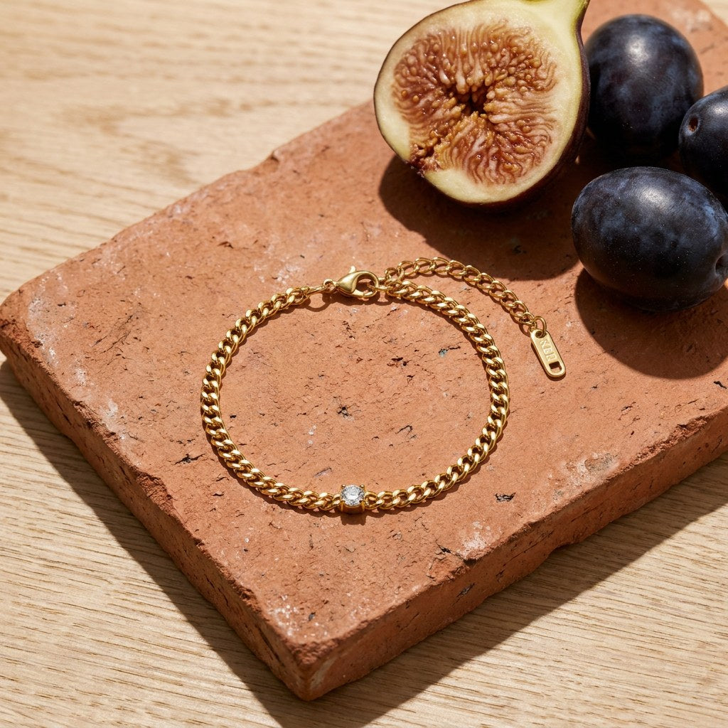 Solitaire Curb Chain Bracelet on a weathered terracotta tile with a cut fig and dark plums