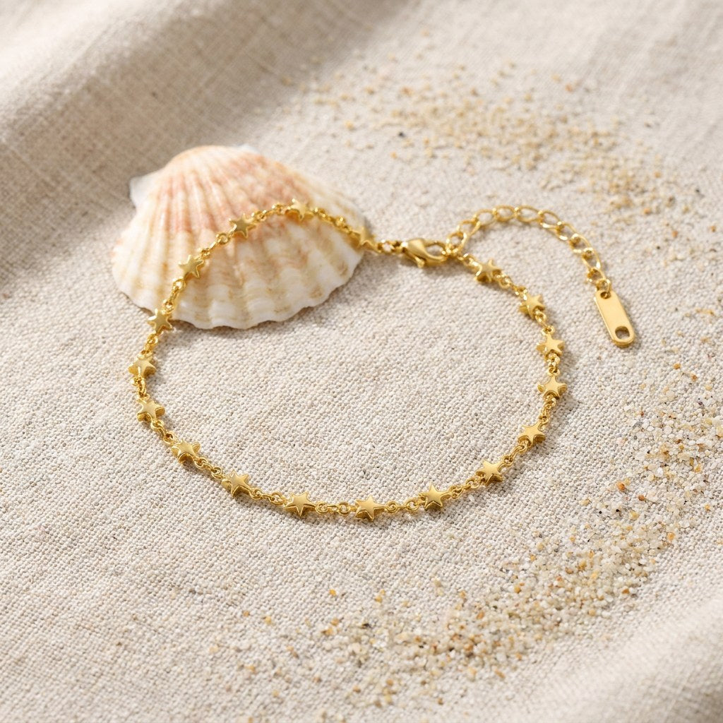 Star Chain Anklet on raw linen beside a scallop shell and a scatter of fine sand
