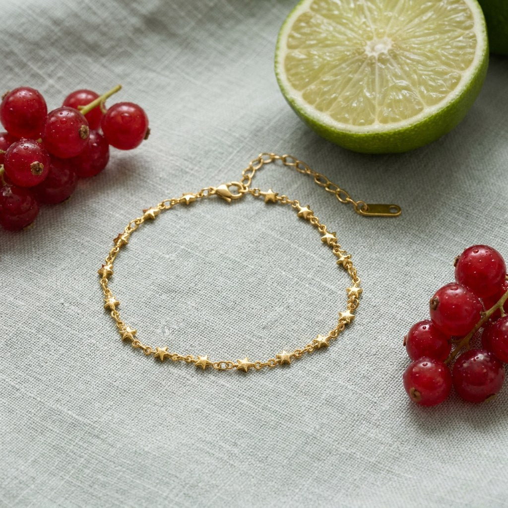 Star Chain Anklet on pale grey-green linen beside a halved lime and red currants