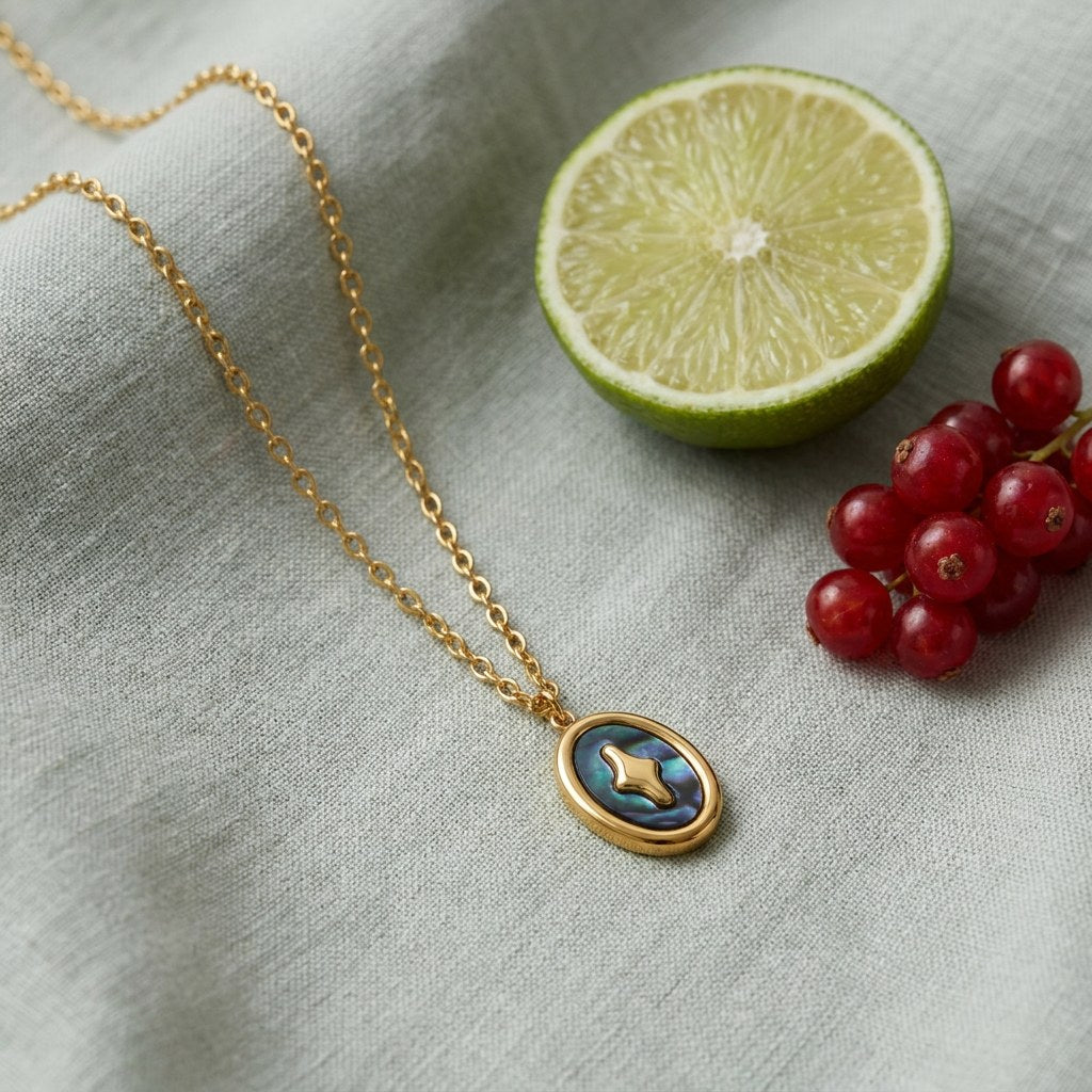 Starry Abalone Pendant Necklace on pale grey-green linen beside a halved lime and red currants