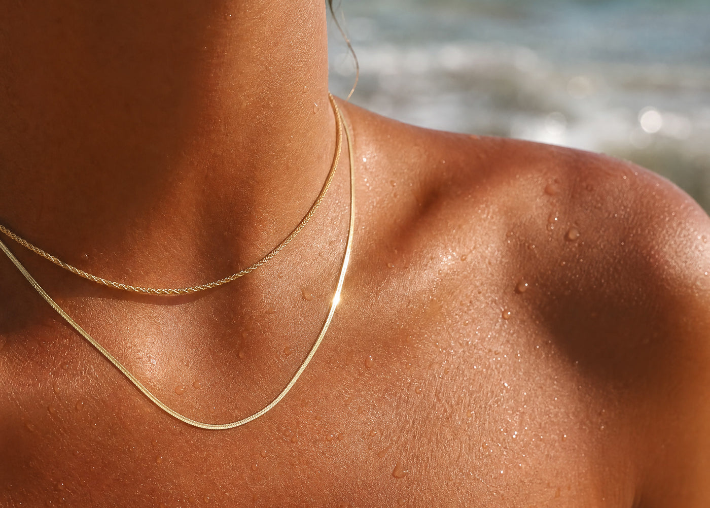 Woman wearing layered Stylr 18k gold-plated 316L chains, wet from the ocean, at the beach