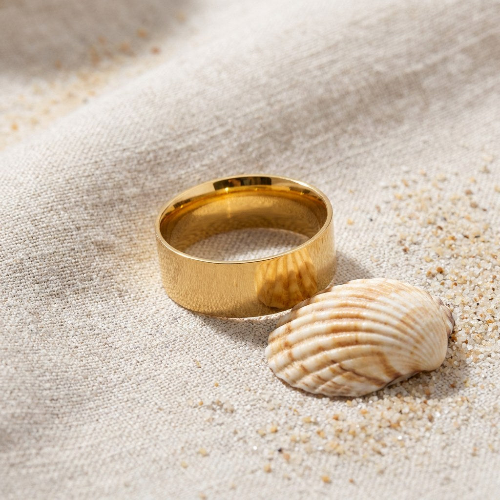 The Band Ring on raw linen beside a scallop shell and a scatter of fine sand