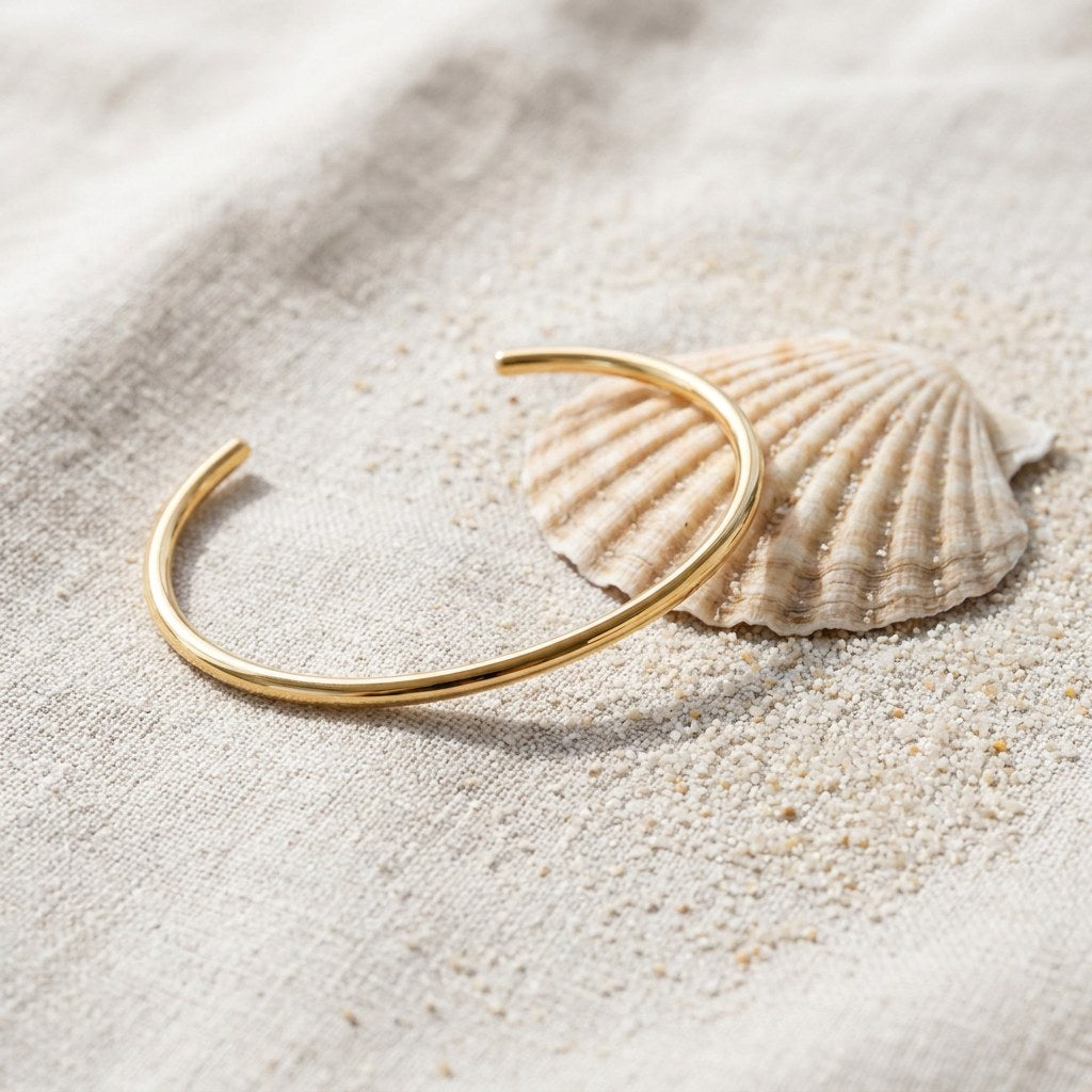 Thin Cuff Bracelet on raw linen beside a scallop shell and a scatter of fine sand
