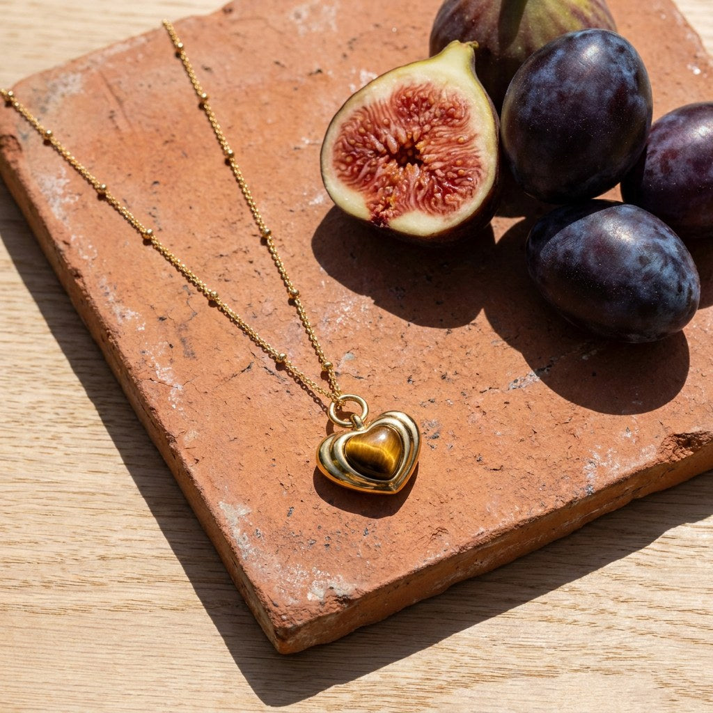 Tiger's Eye Heart Necklace on a weathered terracotta tile with a cut fig and dark plums