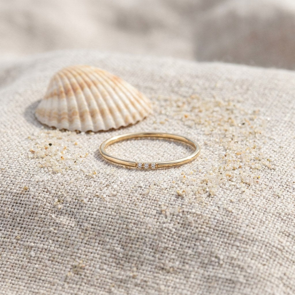 Tiny CZ Stacker Ring on raw linen beside a scallop shell and a scatter of fine sand