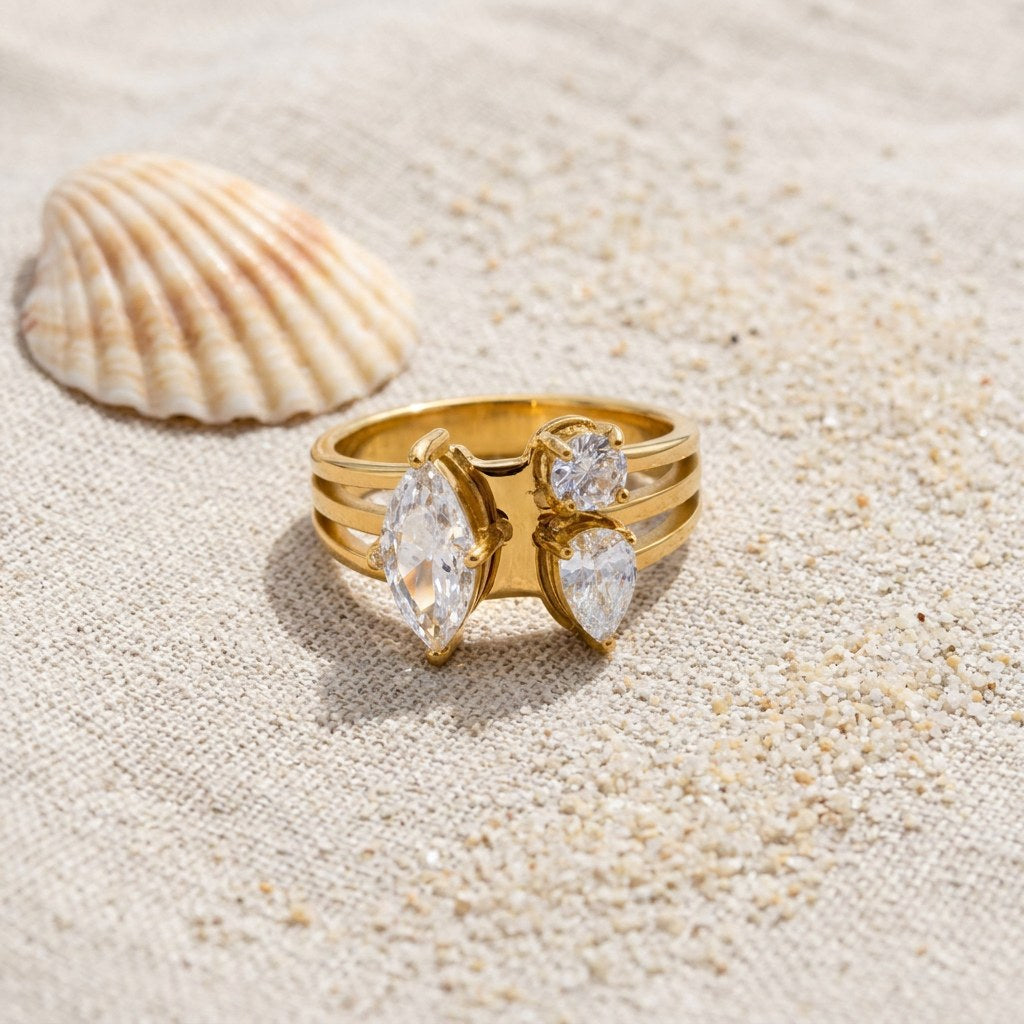 Toi et Moi Cluster Ring on raw linen beside a scallop shell and a scatter of fine sand