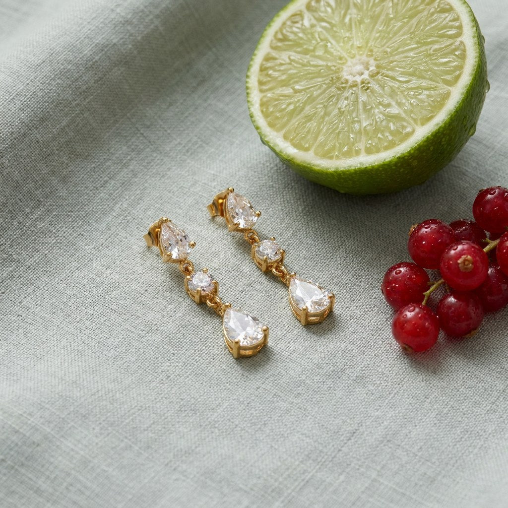 Triple CZ Drop Earrings on pale grey-green linen beside a halved lime and red currants