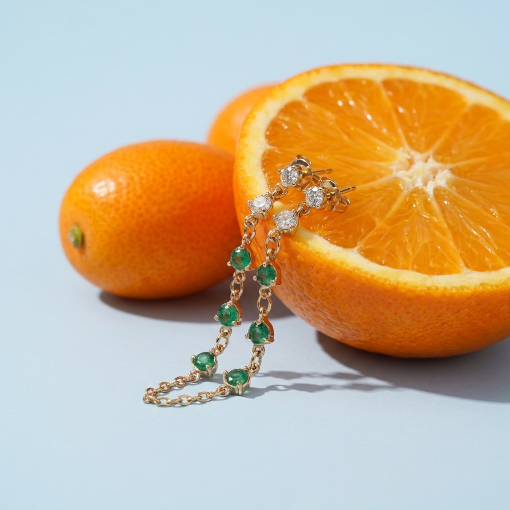 Twinkling Chain Earrings on a pale blue backdrop beside a halved orange and two kumquats