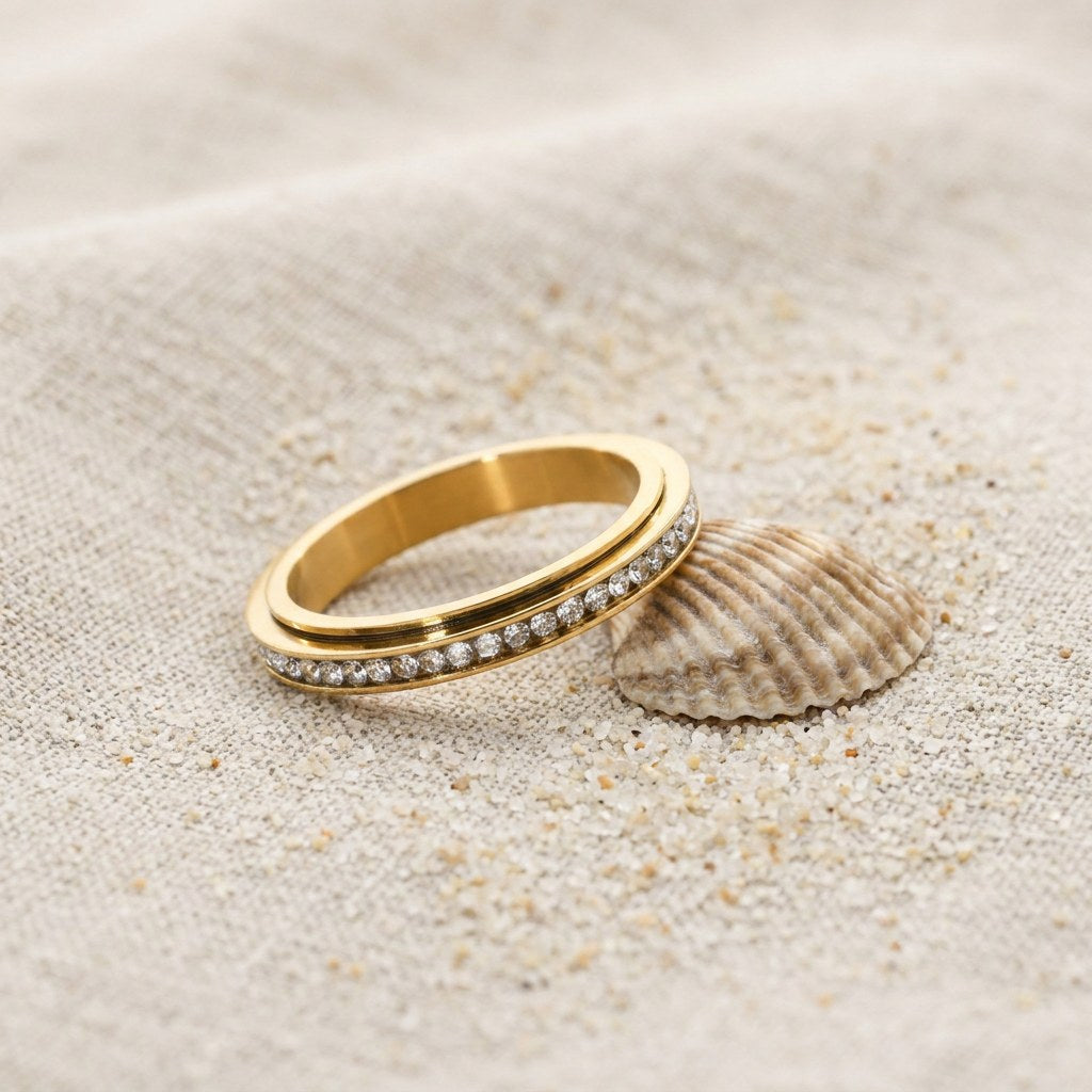 Twinkling Eternity Fidget Ring on raw linen beside a scallop shell and a scatter of fine sand