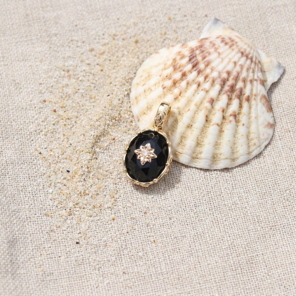 Vintage Black Onyx Starburst Charm on raw linen beside a scallop shell and a scatter of fine sand